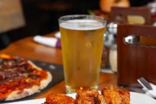 Beer, chicken wings, and pizza on a wooden dining table.