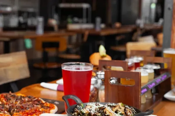 Restaurant table with red drink, pizza, brussels sprouts, and beer flight.
