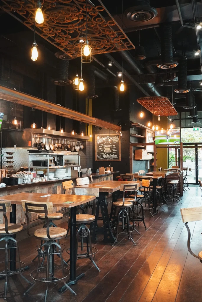 Industrial-chic restaurant interior with open kitchen, warm lighting, and high-top tables.