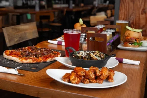 Restaurant table with pizza, wings, burger, vegetables, and a beer flight.