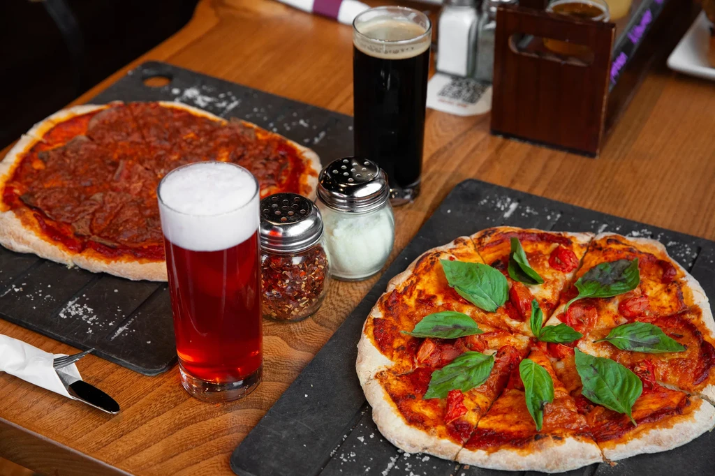Two fresh pizzas and two beers on a light wooden table.