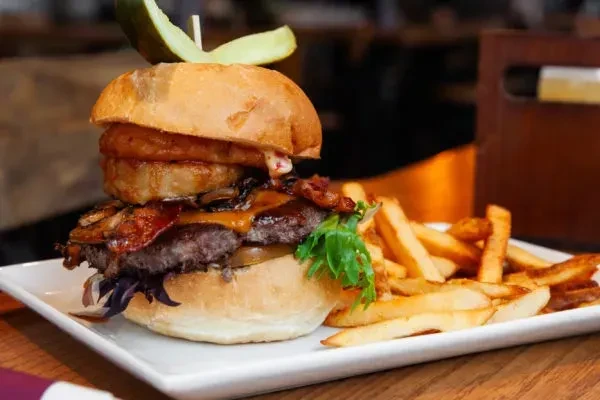 Close-up: Layered gourmet burger, pickle spear, and golden french fries.