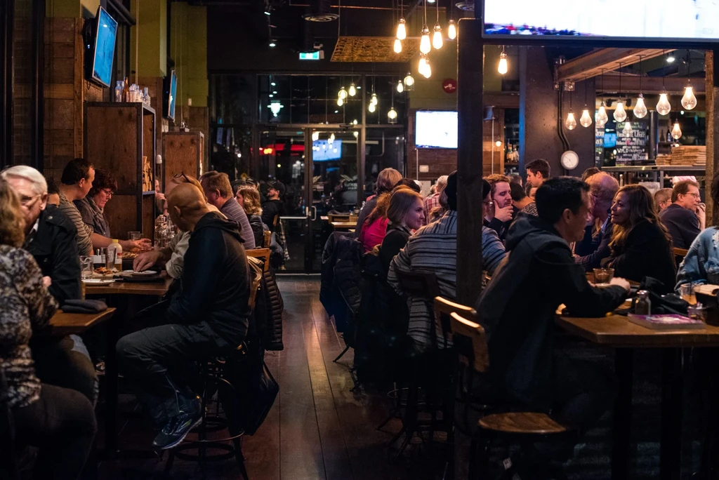 Bustling restaurant interior with diners and warm Edison-style lighting.