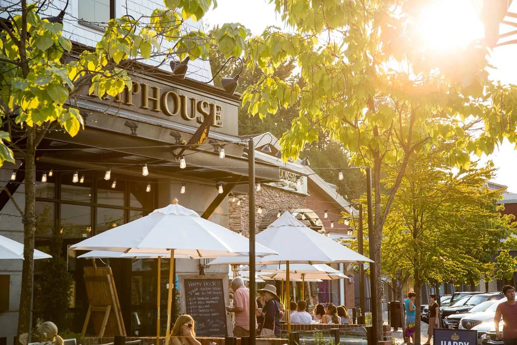 TAPHOUSE restaurant patio with patrons under umbrellas in golden sunlight.