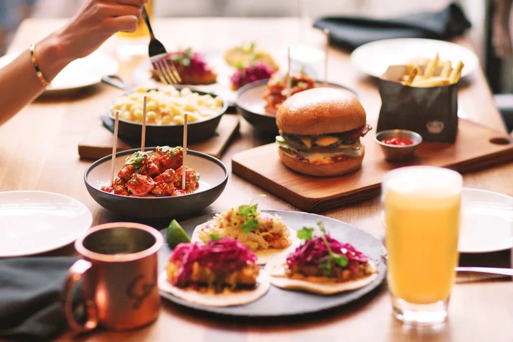 Restaurant table with burger, fries, tacos, mac and cheese, and beer.