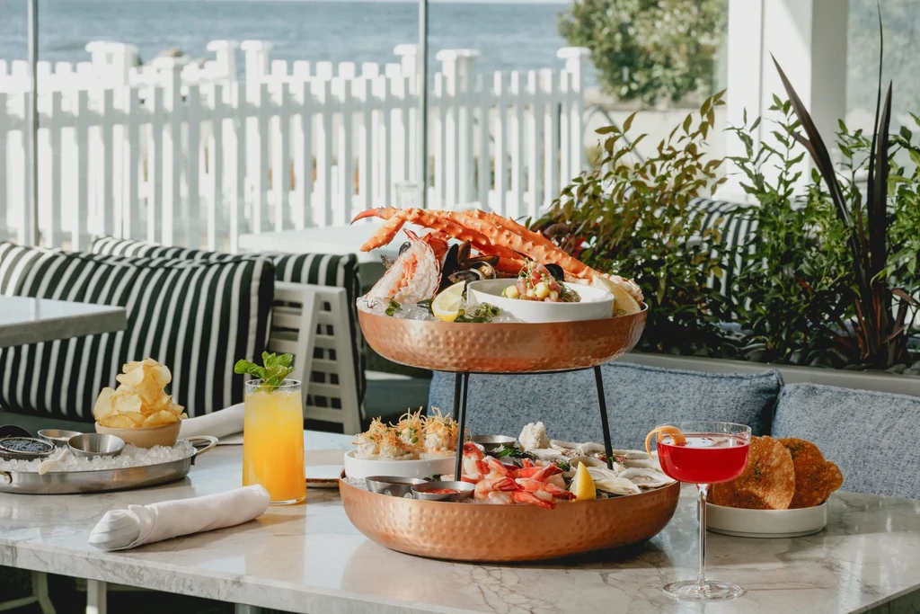 Two-tiered copper seafood tower, cocktails, chips on a waterfront restaurant table.