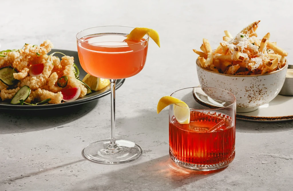 Flat lay of fried calamari, two cocktails, and cheesy french fries.