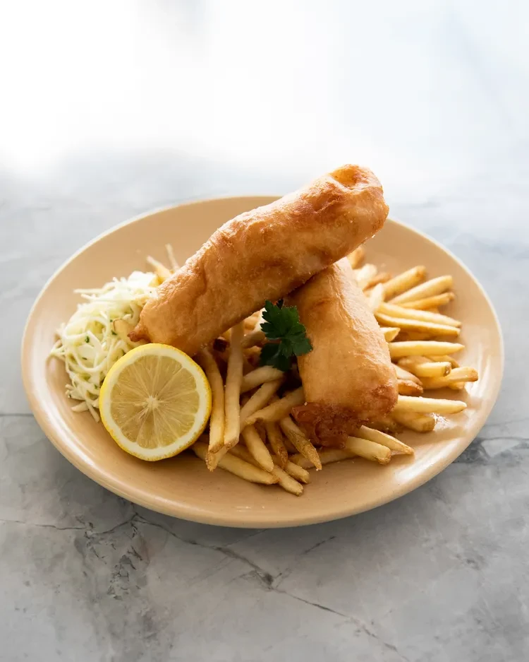 Plate of golden-brown fish and chips, lemon, and coleslaw.