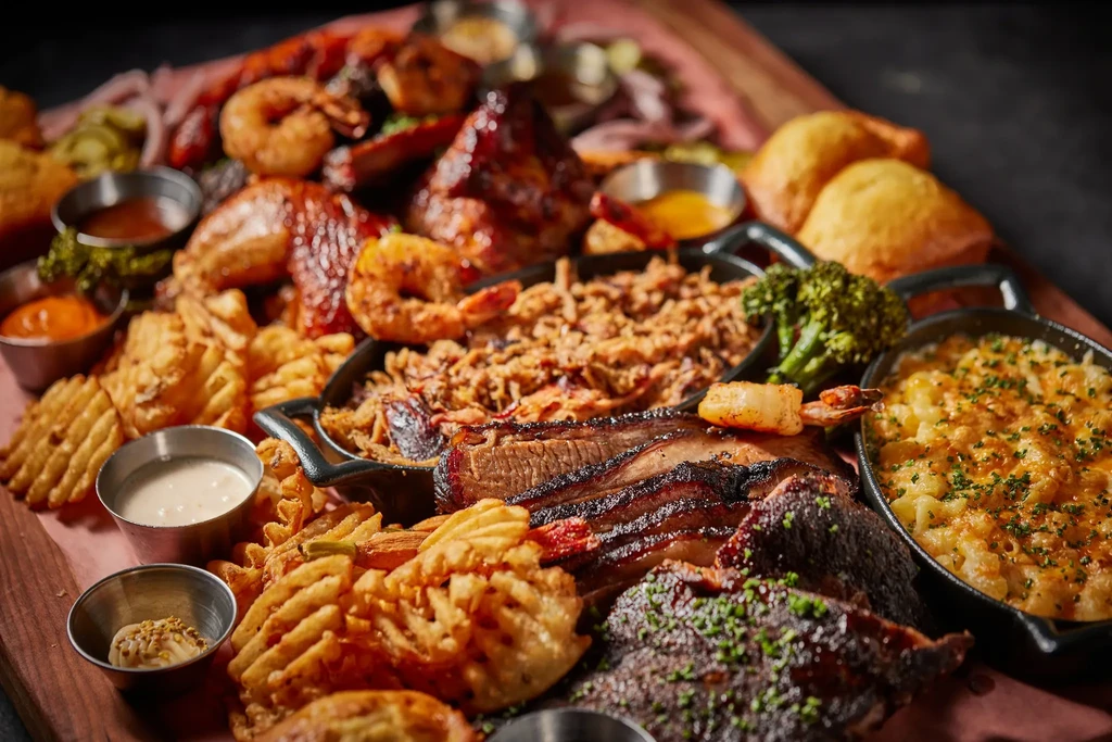 BBQ platter on wood board with meats, fries, mac & cheese.