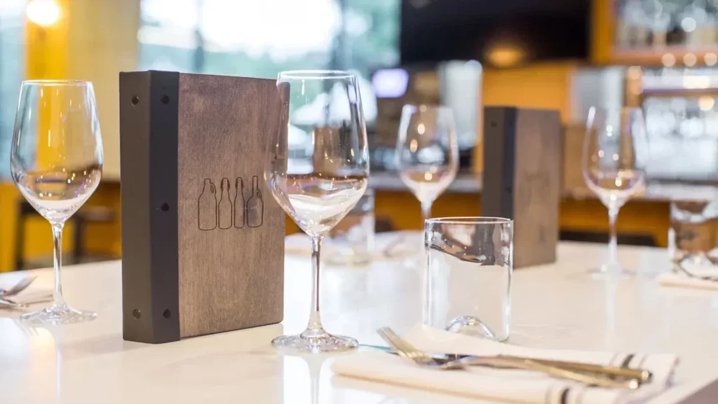 Empty wine glasses, cutlery, and bottle-etched menus on a clean restaurant table.