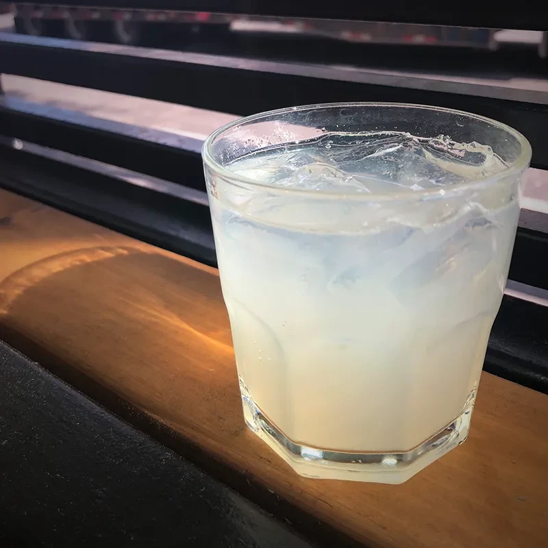 Faceted glass with a cloudy drink, ice, and condensation on wood.
