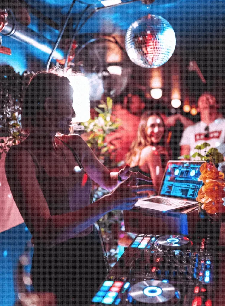 Woman DJ operates mixing console and laptop in a vibrant club.