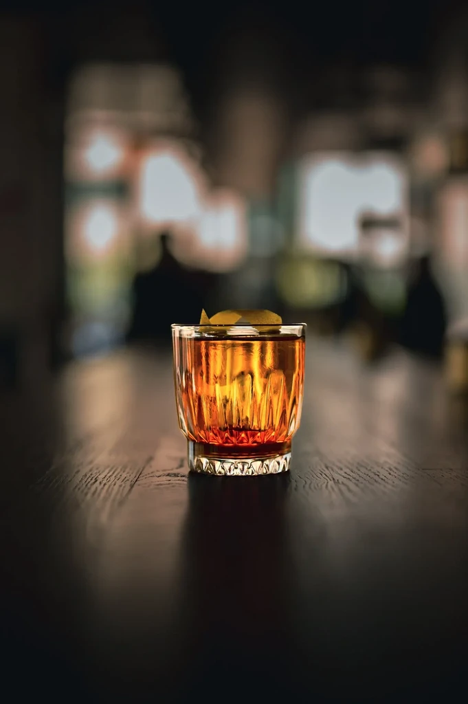 Amber cocktail in textured glass with citrus peel on wood.