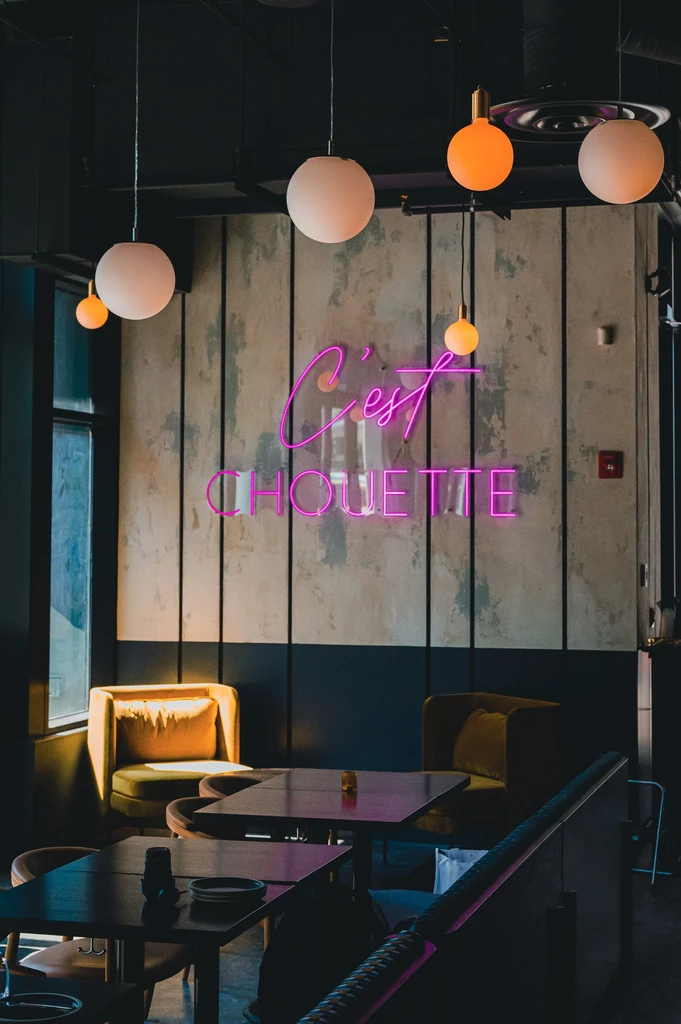 Dimly lit modern restaurant with magenta "C'est CHOUETTE" neon sign.