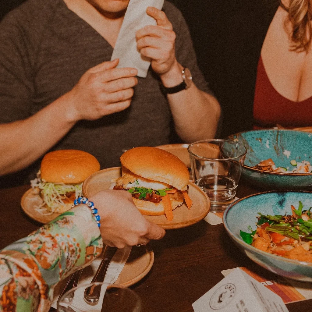 Two burgers and other dishes on a warmly lit restaurant table.