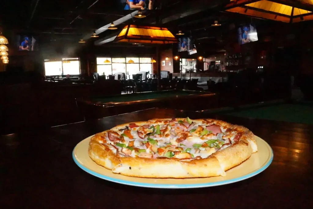 Close-up of generously topped pizza in a dimly lit sports bar.