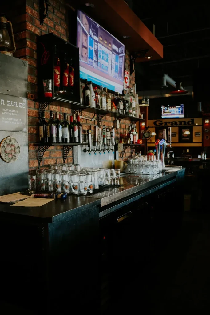 Dimly lit bar counter with beer taps, liquor, brick wall, and TV.