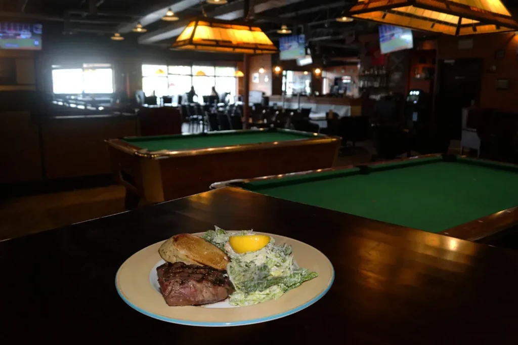 Close-up of steak, Caesar salad, and toast in a casual sports bar.