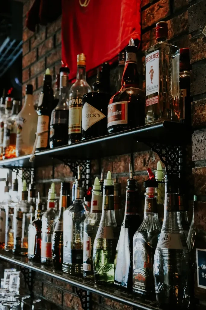 Liquor bottles with pour spouts on bar shelves against a brick wall.