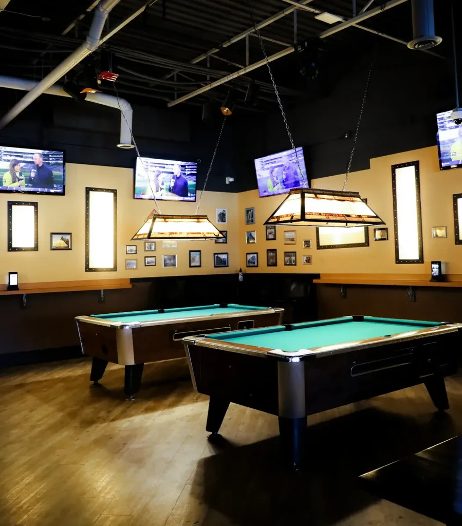 Two teal felt pool tables brightly lit by overhead stained-glass lamps.