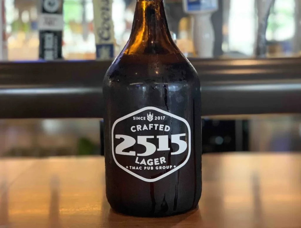 Close-up of a condensing amber '2515 LAGER' bottle on a bar top.