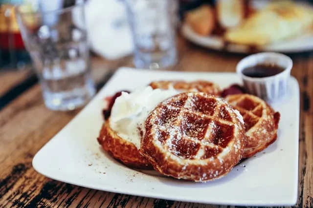 Close-up of two waffles with whipped cream, powdered sugar, and syrup.