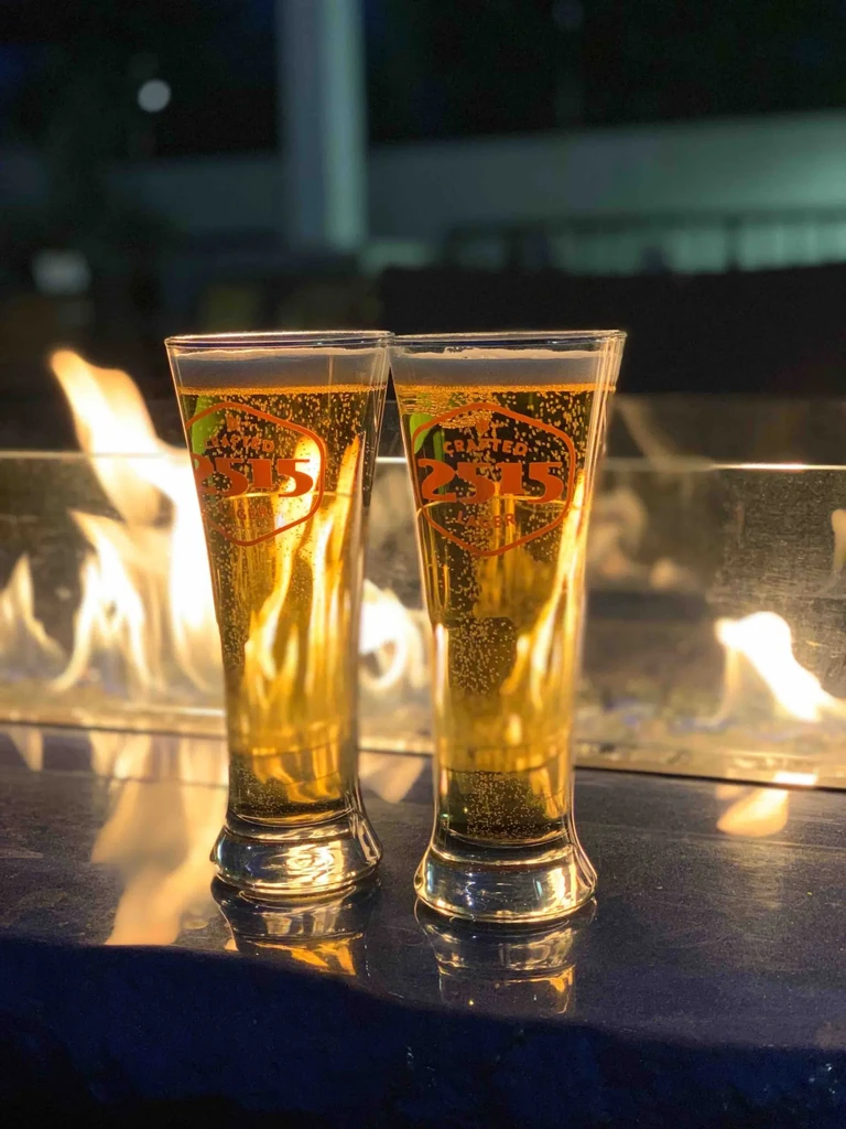Two glasses of 'CRAFTED 2315 BEER' in front of a warm fire.