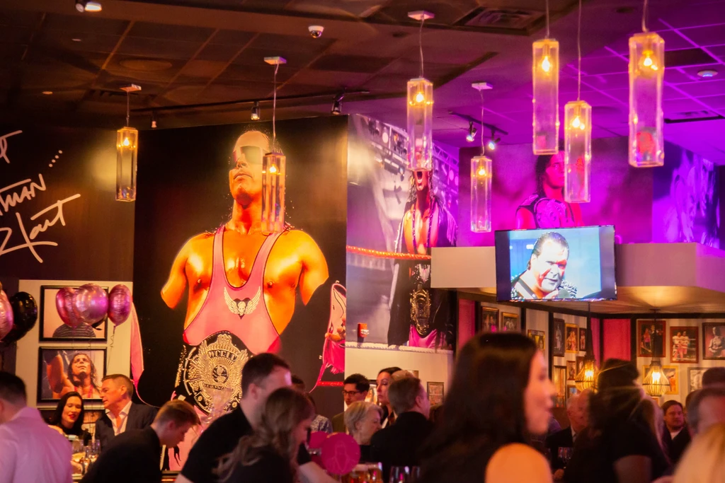 Busy wrestling-themed restaurant interior with Bret Hart mural and purple lights.