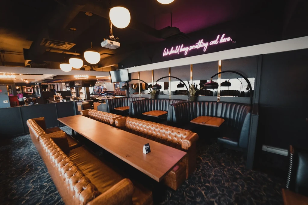 Modern restaurant interior with tufted bench, dark booths, and pink neon sign.
