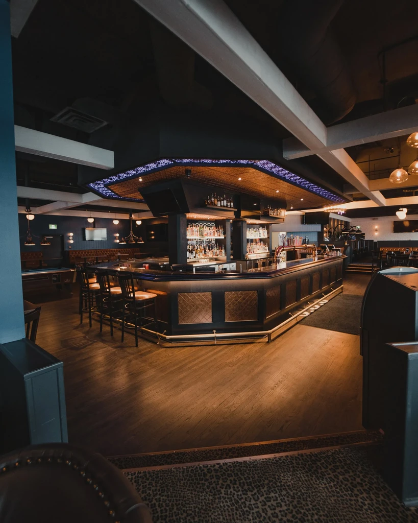 Upscale U-shaped bar interior with bottles, purple lights, and patterned ceiling.