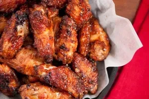 Golden-brown, glazed chicken wings with sesame seeds in a black bowl.
