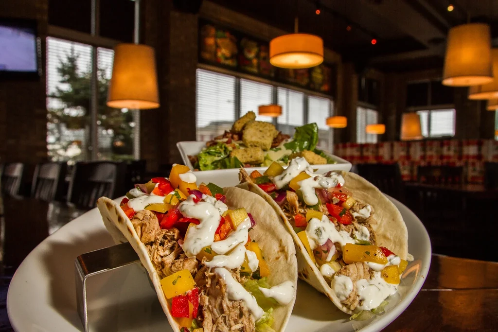 Two vibrant tacos with meat and peppers, salad, in a warm restaurant.