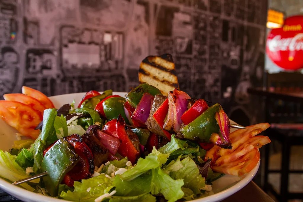 Grilled meat and vegetable skewer with salad, tomatoes, and bread.