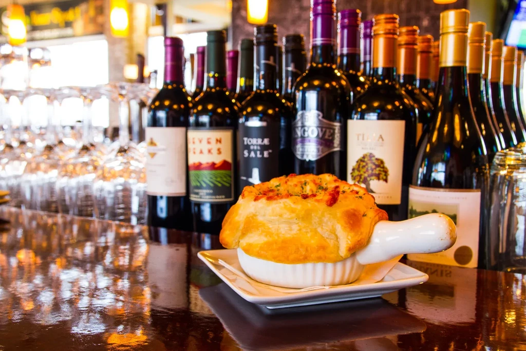 Savory pot pie with flaky golden crust, wine bottles in background.