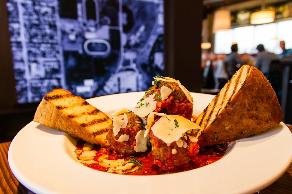 Three large meatballs with red sauce, cheese, herbs, grilled bread.