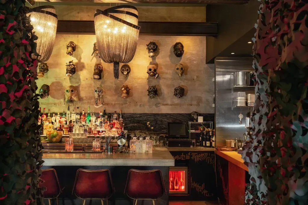 Bar interior featuring unique gas mask wall art and a well-stocked counter.