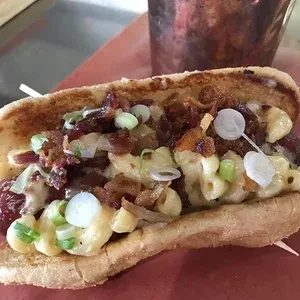 Toasted bun hot dog with macaroni and cheese, bacon, and green onions.