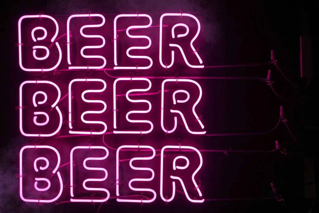 Vibrant pinkish-purple neon sign spells 'BEER' three times vertically.