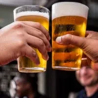 Two hands clinking cold, frothy golden beer glasses.