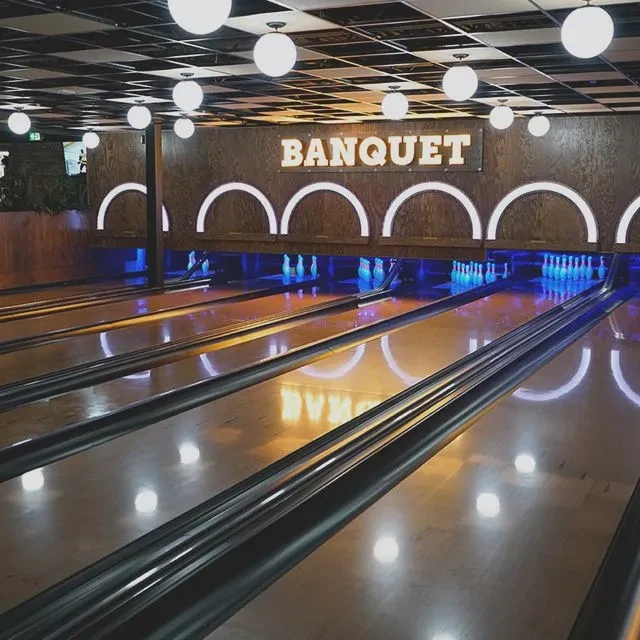 Modern bowling alley with blue-lit lanes and a "BANQUET" sign.