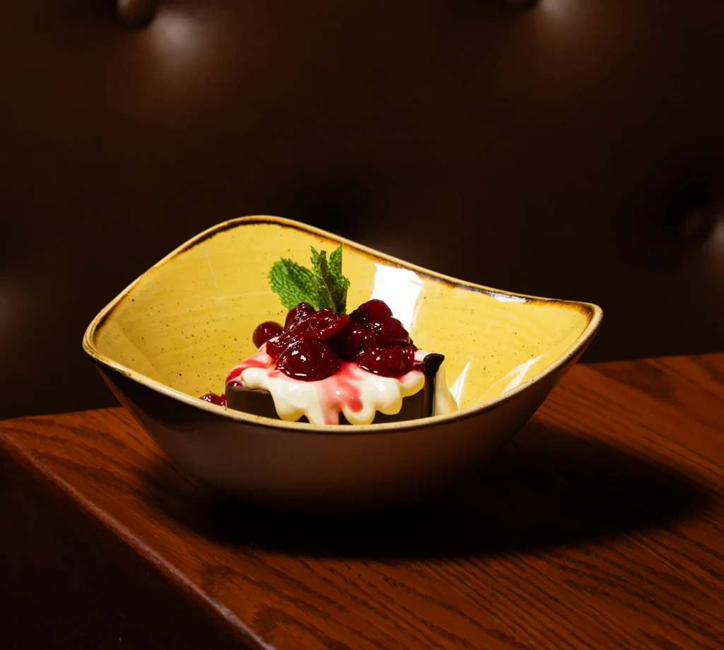 Dark dessert with cream, berry compote, and mint in ochre bowl.