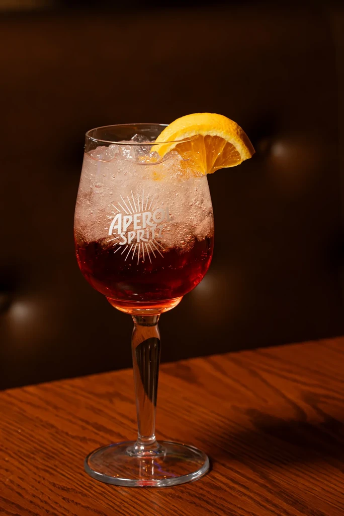 Vibrant Aperol Spritz cocktail with ice and orange slice in branded glass.