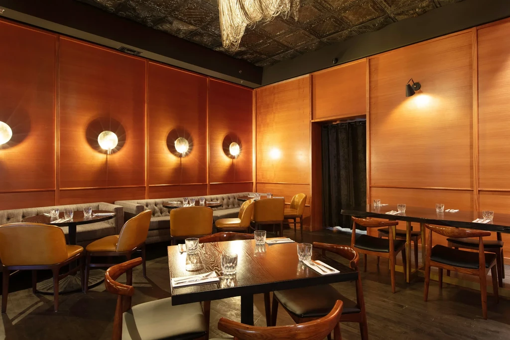 Warmly lit, elegant restaurant dining room with wood panels and plush seating.