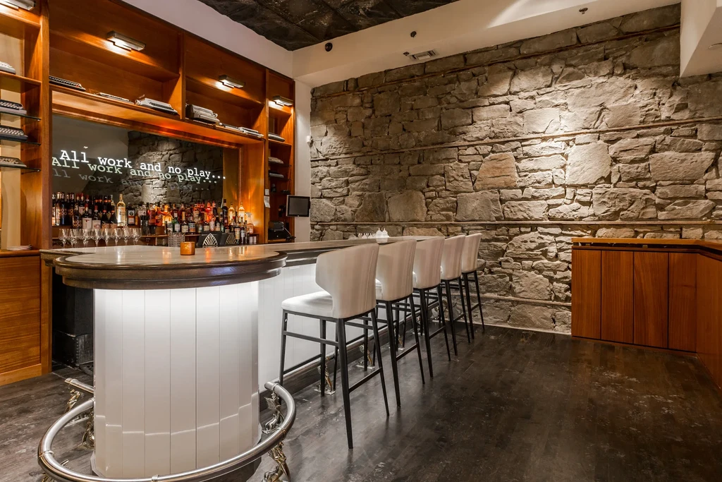 Modern rustic bar with wooden counter, stone wall, five stools, liquor.