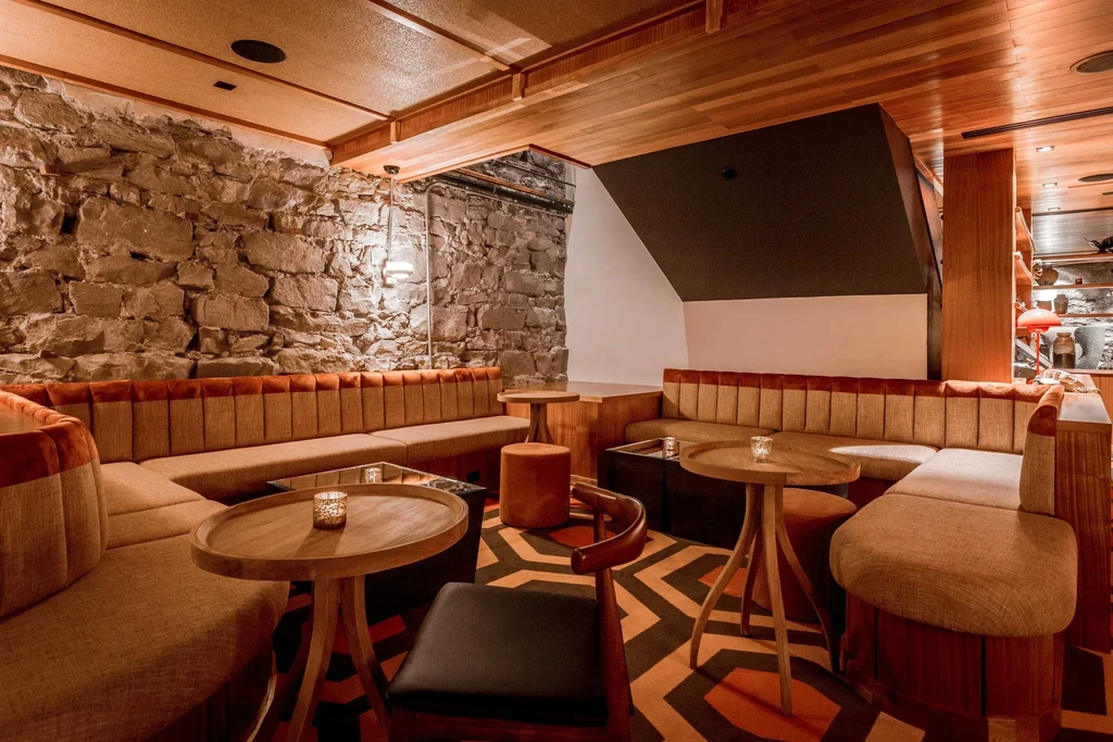 Cozy, modern rustic restaurant interior with stone wall and banquettes.
