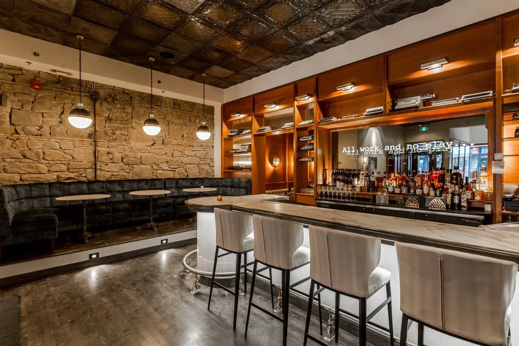 Stylish bar interior with marble bar, tufted banquette, and stone wall.