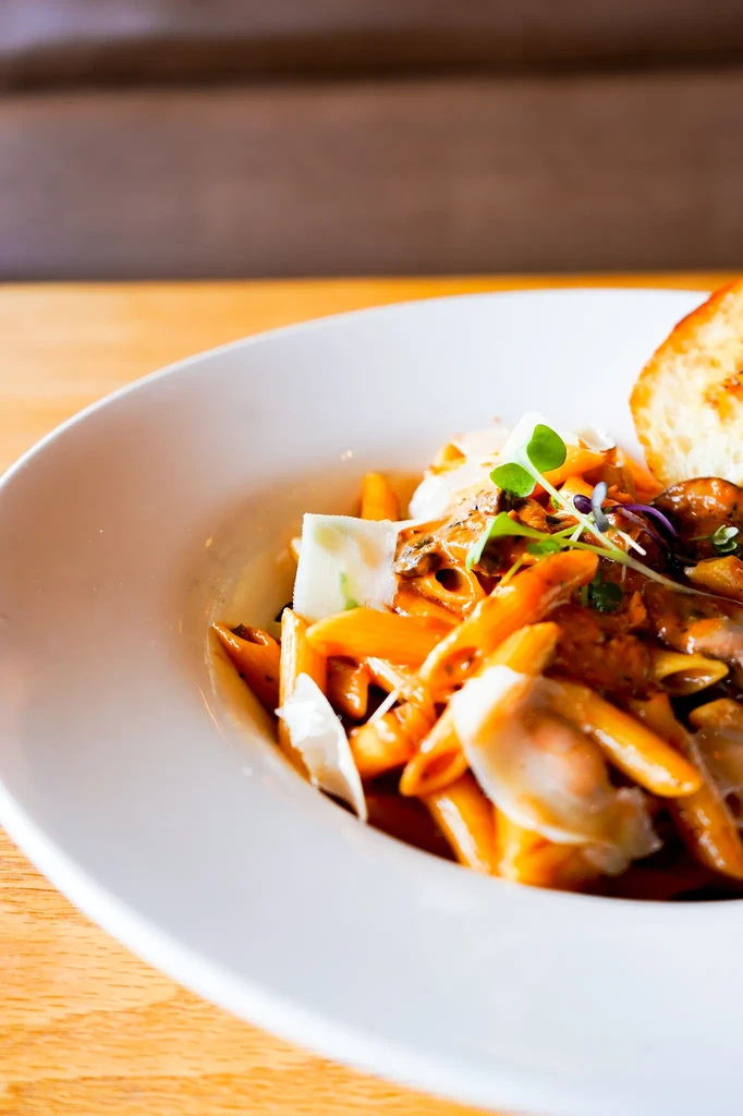 Close-up of penne pasta with sauce, Parmesan, microgreens, and toast.