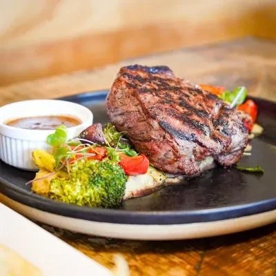 Plated grilled medium-rare steak, colorful vegetables, yellow puree, dark sauce.