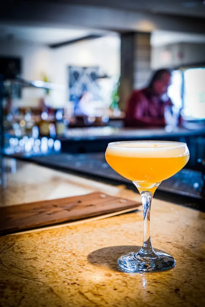 Orange cocktail with foam in a coupe glass on a bar.