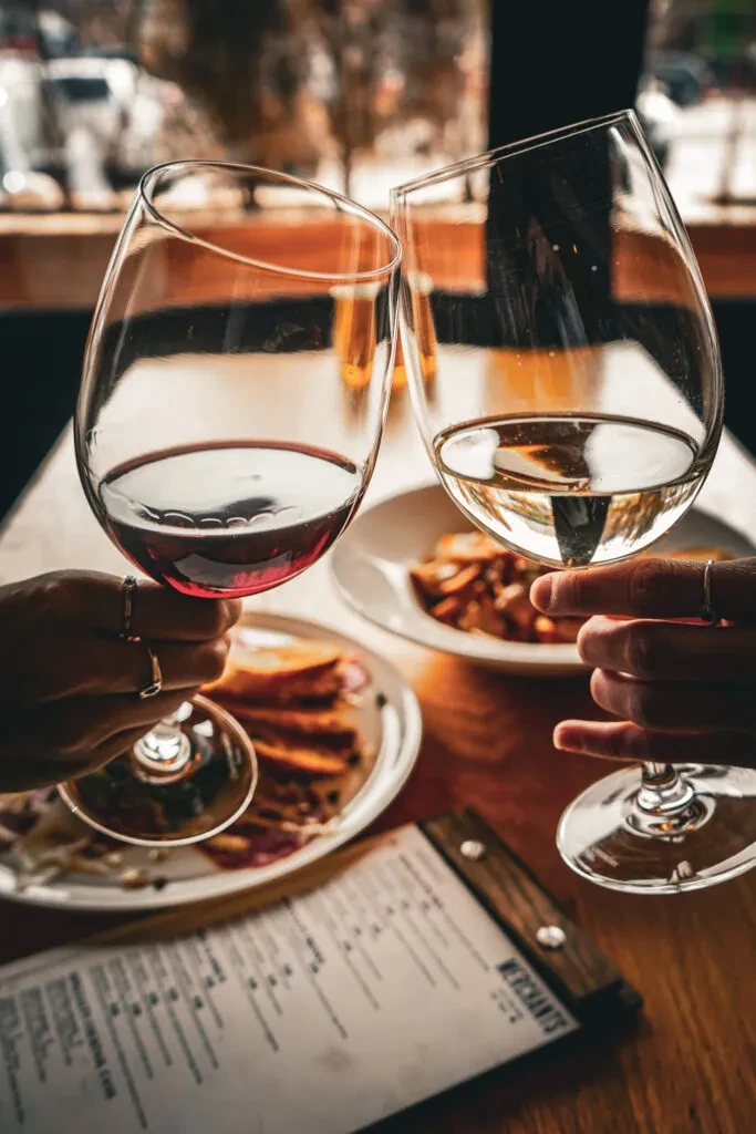 Hands toasting red and white wine glasses at a restaurant.